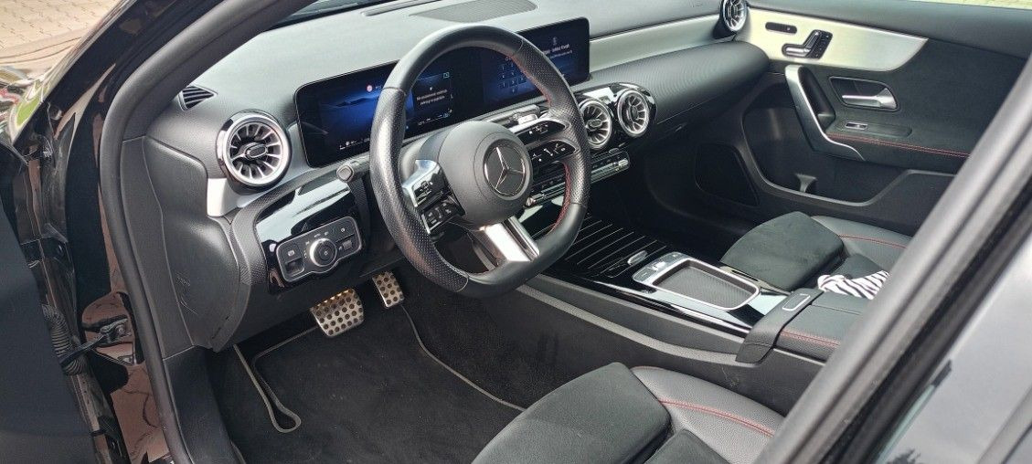 Wnętrze czarnego samochodu marki Mercedes-Benz z widoczną deską rozdzielczą, kierownicą, fotelami oraz srebrnymi detalami wykończenia.