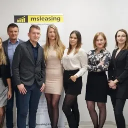 Grupa pracowników firmy leasingowej pozuje na tle roll-upu z logo firmy, prezentując zróżnicowany dress code.