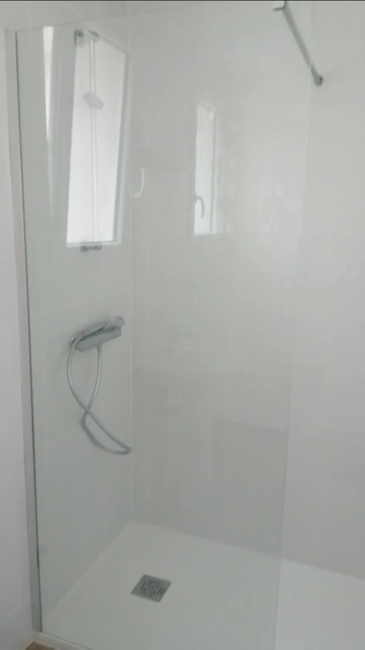 Nowoczesna kabina prysznicowa z białymi ścianami, szklanymi drzwiami i chromowaną armaturą, widok na odpływ liniowy w brodziku.