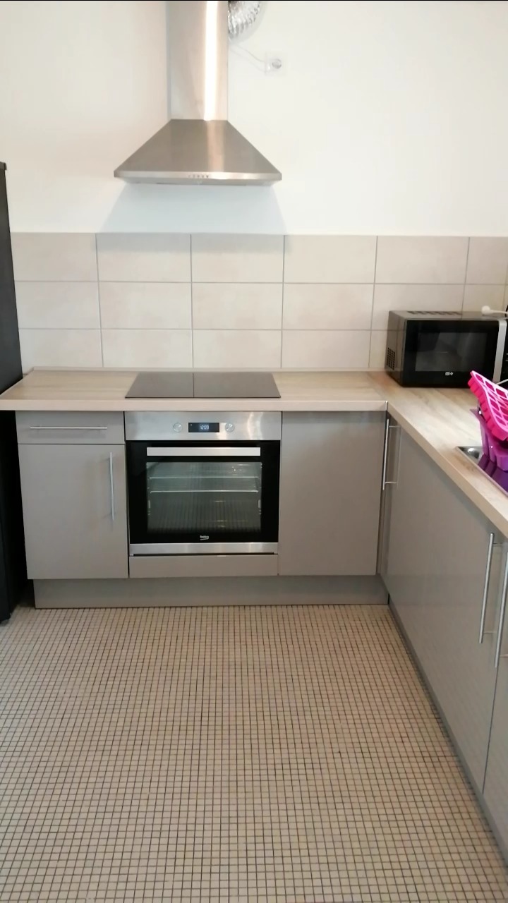 Wykończona kuchnia w szarościach z płytkami podłogowymi w kratkę, zabudową kuchenną z piekarnikiem i płytą indukcyjną, okapem oraz mikrofalówką.