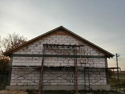 Budynek w trakcie budowy z białych bloczków, widoczne rusztowania i surowa konstrukcja dachu.