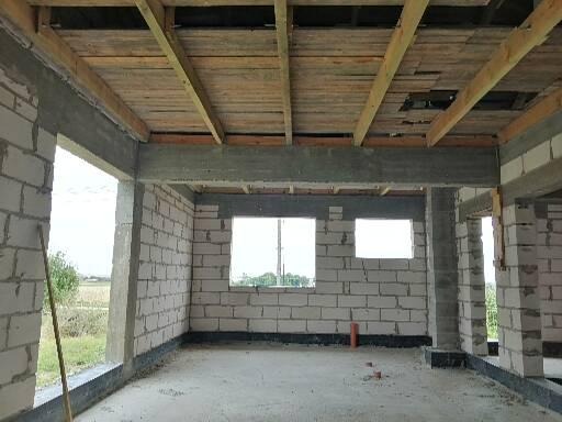 Surowy stan wnętrza budynku z pustaków, widoczne drewniane elementy stropu i betonowe nadproża okienne.