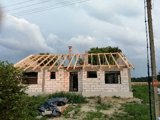 Budowa domu jednorodzinnego w trakcie wznoszenia więźby dachowej, widoczne bloczki z betonu komórkowego, drewniana konstrukcja dachu, słup energetyczny z numerem 160 w tle.