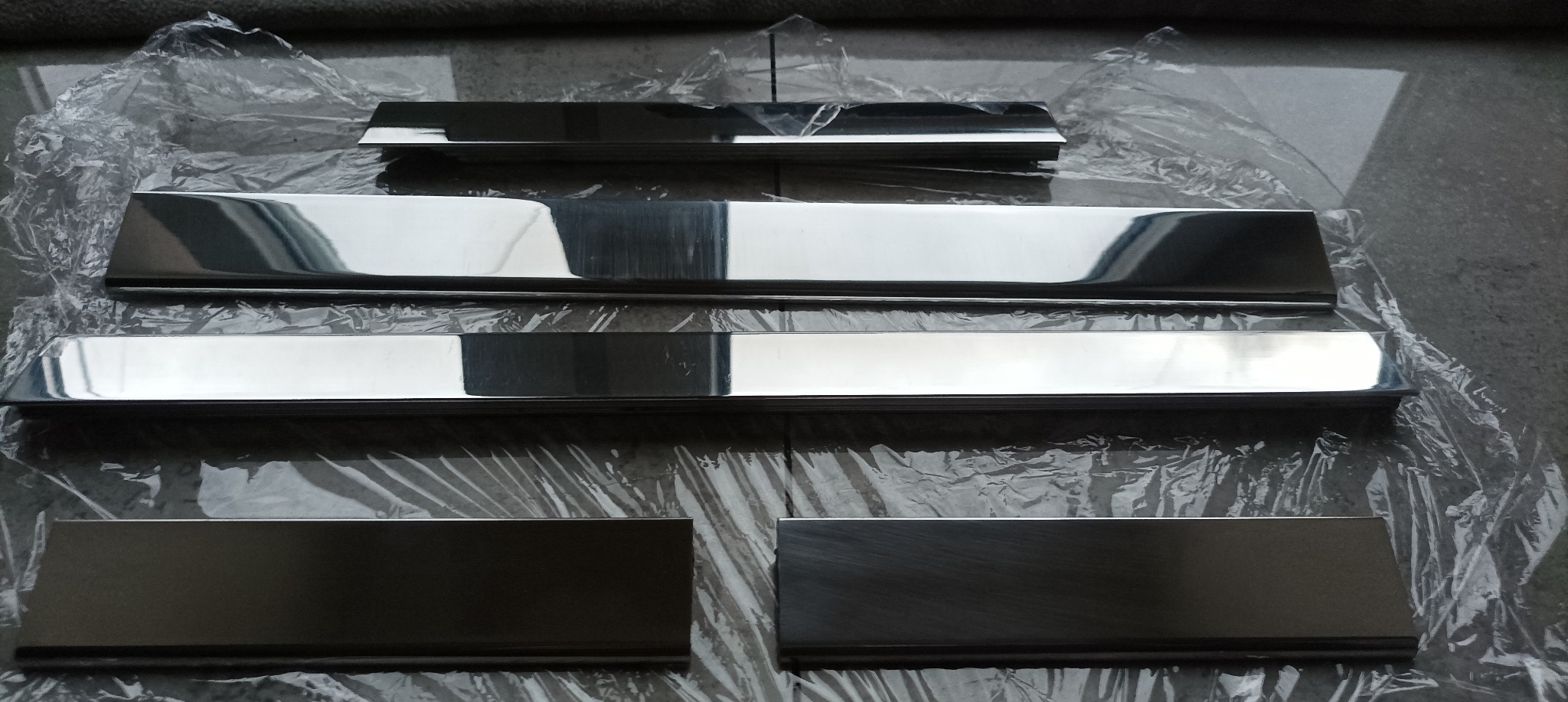 Polerowane, prostokątne metalowe elementy o różnej grubości, ułożone na folii ochronnej, prawdopodobnie przygotowane do montażu.