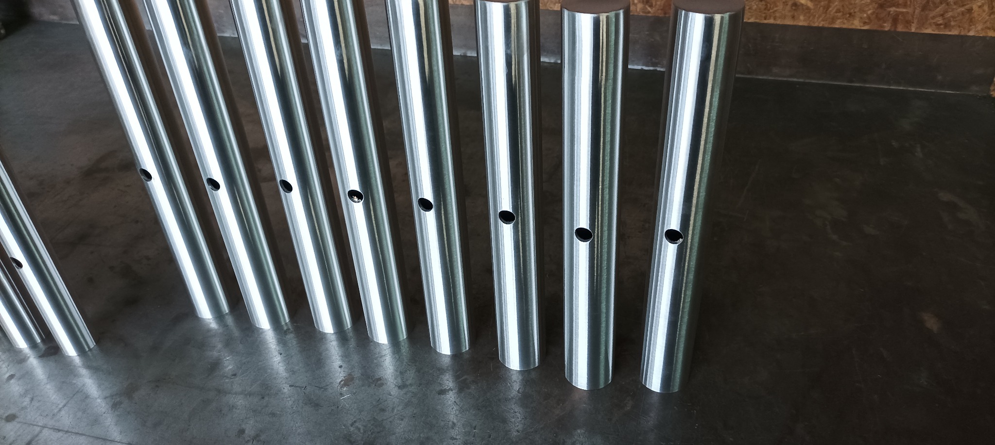 Rząd obrobionych, błyszczących, metalowych prętów z nawierconymi otworami, ustawionych pionowo na metalowej powierzchni roboczej.