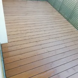 Nowoczesny taras z desek w odcieniach brązu, z metalową balustradą o ażurowym wzorze, widok z góry pod lekkim kątem.