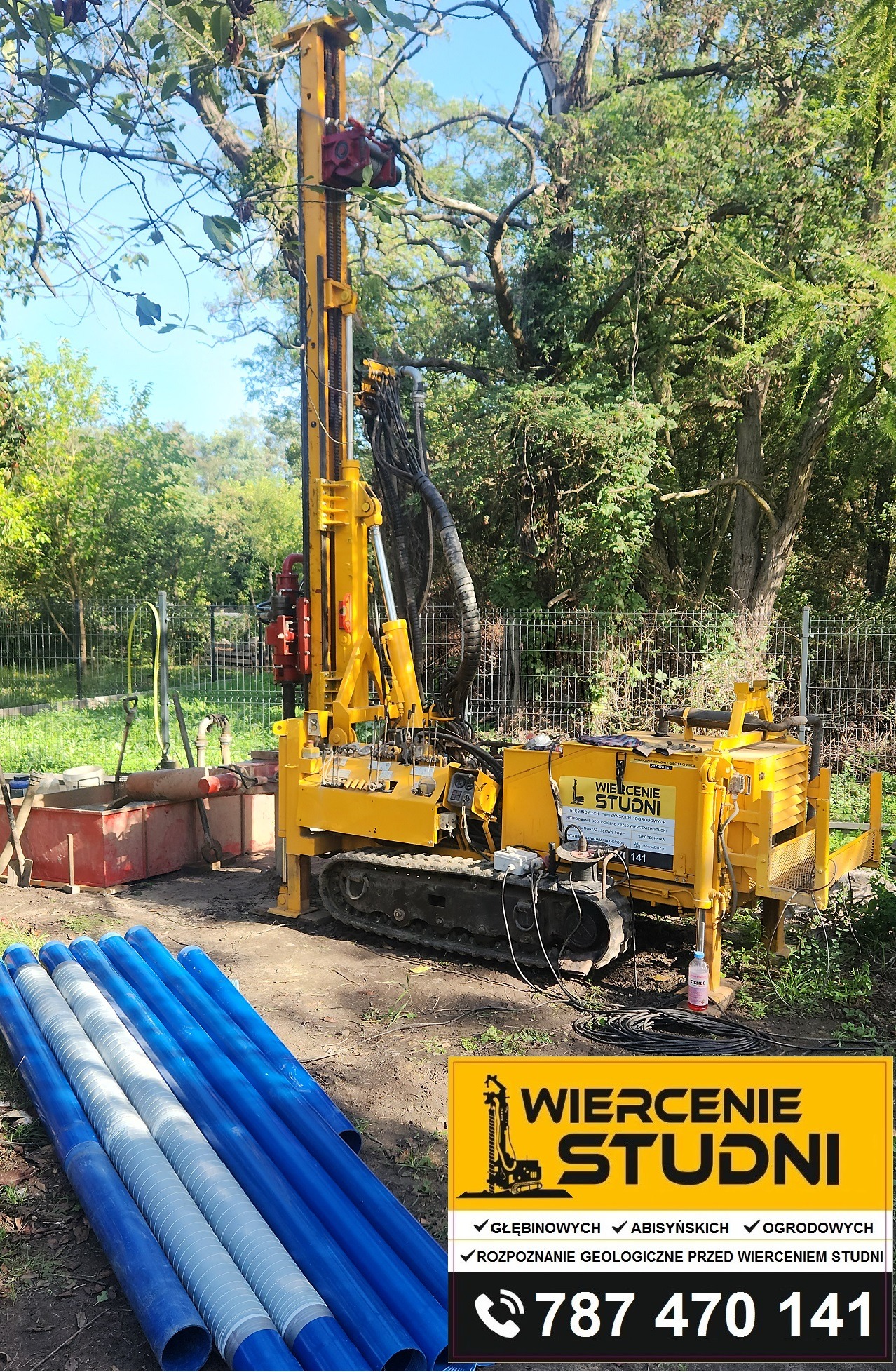 Żółta wiertnica na gąsienicach, rury studzienne w tle, teren zielony. Wiertnica gotowa do pracy, widoczny osprzęt i przewody. Reklama firmy na maszynie.