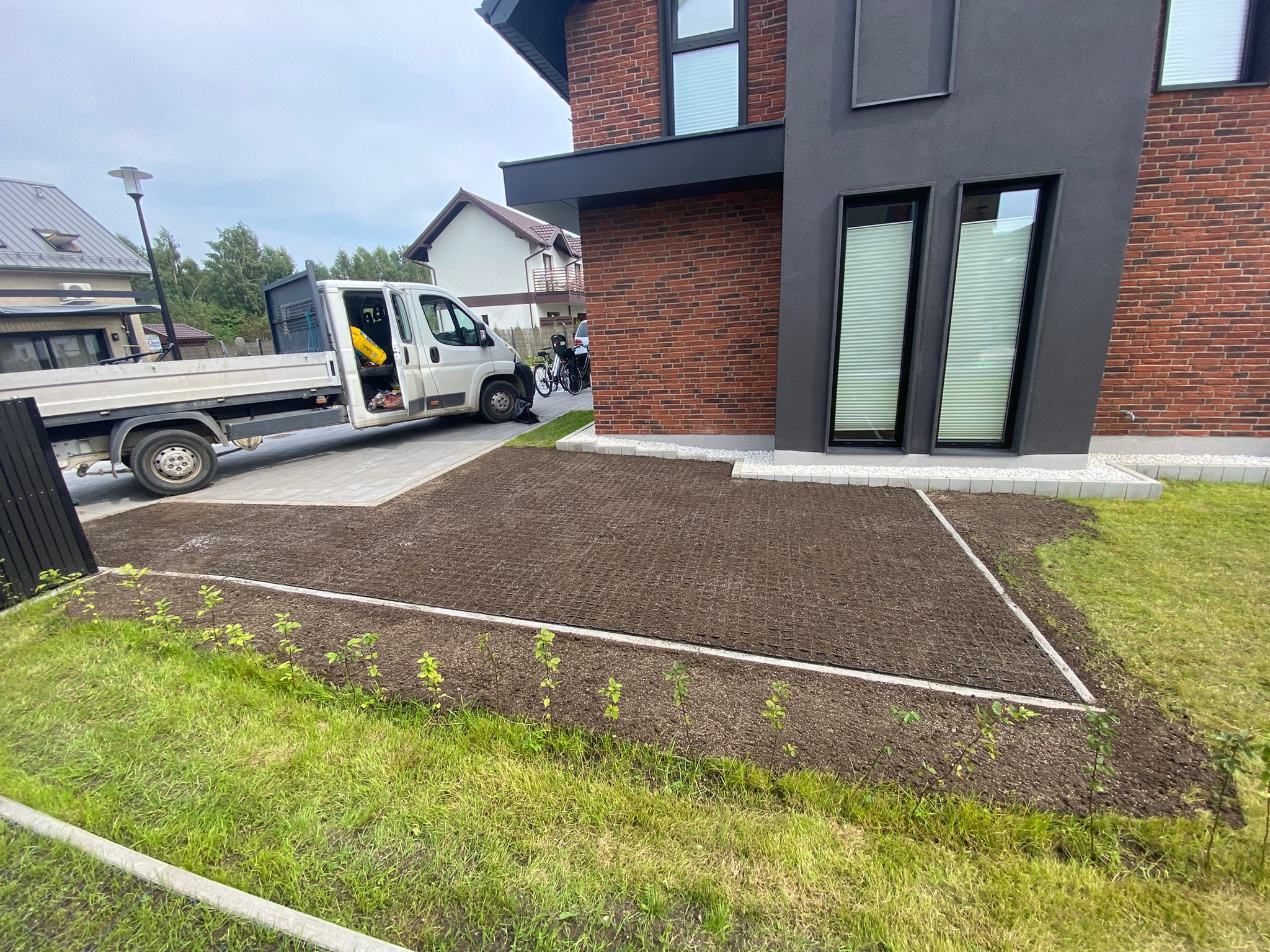 Przygotowany teren pod trawnik w Karwi, z widoczną siatką wzmacniającą i dostawczym samochodem na posesji nowoczesnego domu z cegły.