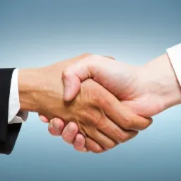 Uścisk dłoni: jasna dłoń w białej koszuli ściska ciemniejszą dłoń w czarnym garniturze na tle gradientu błękitu.