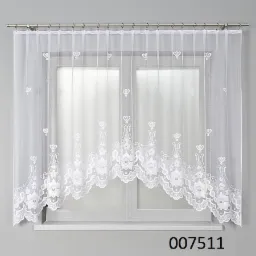 Biała, koronkowa firanka na karniszu, z motywem kwiatowym, przysłaniająca okno z białymi ramami i parapetem.