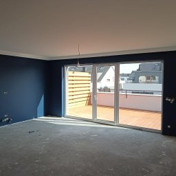 Gambud - Wnętrze pokoju po malowaniu ścian na ciemny granat, z widocznymi puszkami elektrycznymi i wyjściem na balkon z drewnianą podłogą i balustradą.