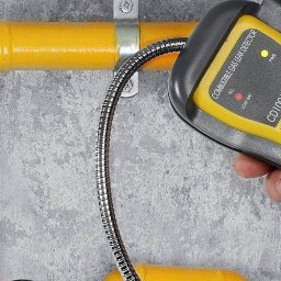 Serwis Gazowy - Sprawdzanie szczelności żółtej instalacji gazowej za pomocą detektora nieszczelności gazu, model CD100A, na tle szarej ściany.