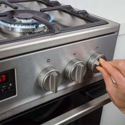 Serwis Gazowy - Dłoń reguluje pokrętło kuchenki gazowej Gorenje z palnikiem włączonym na płycie ze stali nierdzewnej, widoczny wyświetlacz cyfrowy.