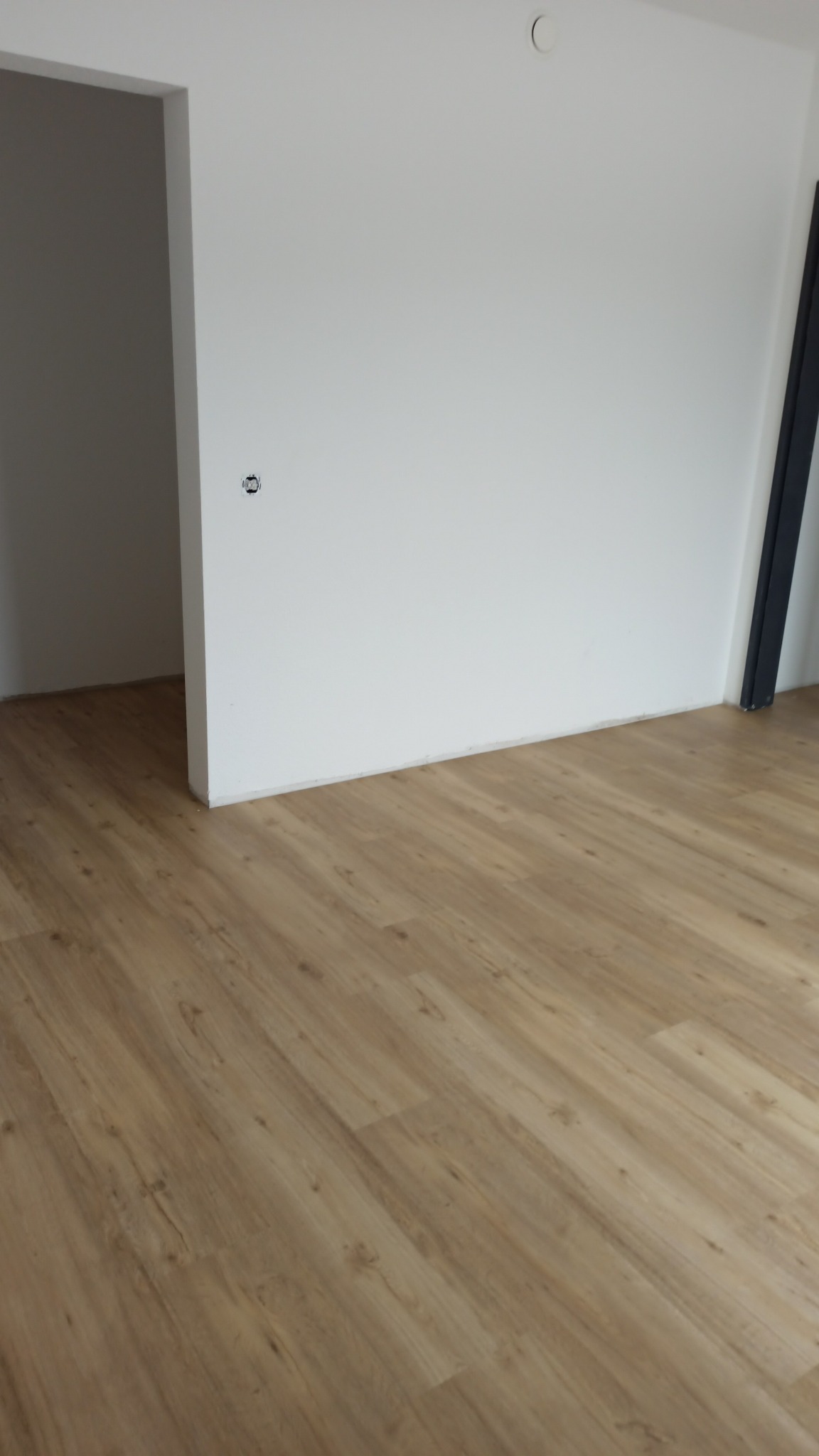 Jasna, drewnopodobna podłoga ułożona w nowym mieszkaniu w Gorzowie Wielkopolskim, widok na białe ściany i wejście do innego pomieszczenia.