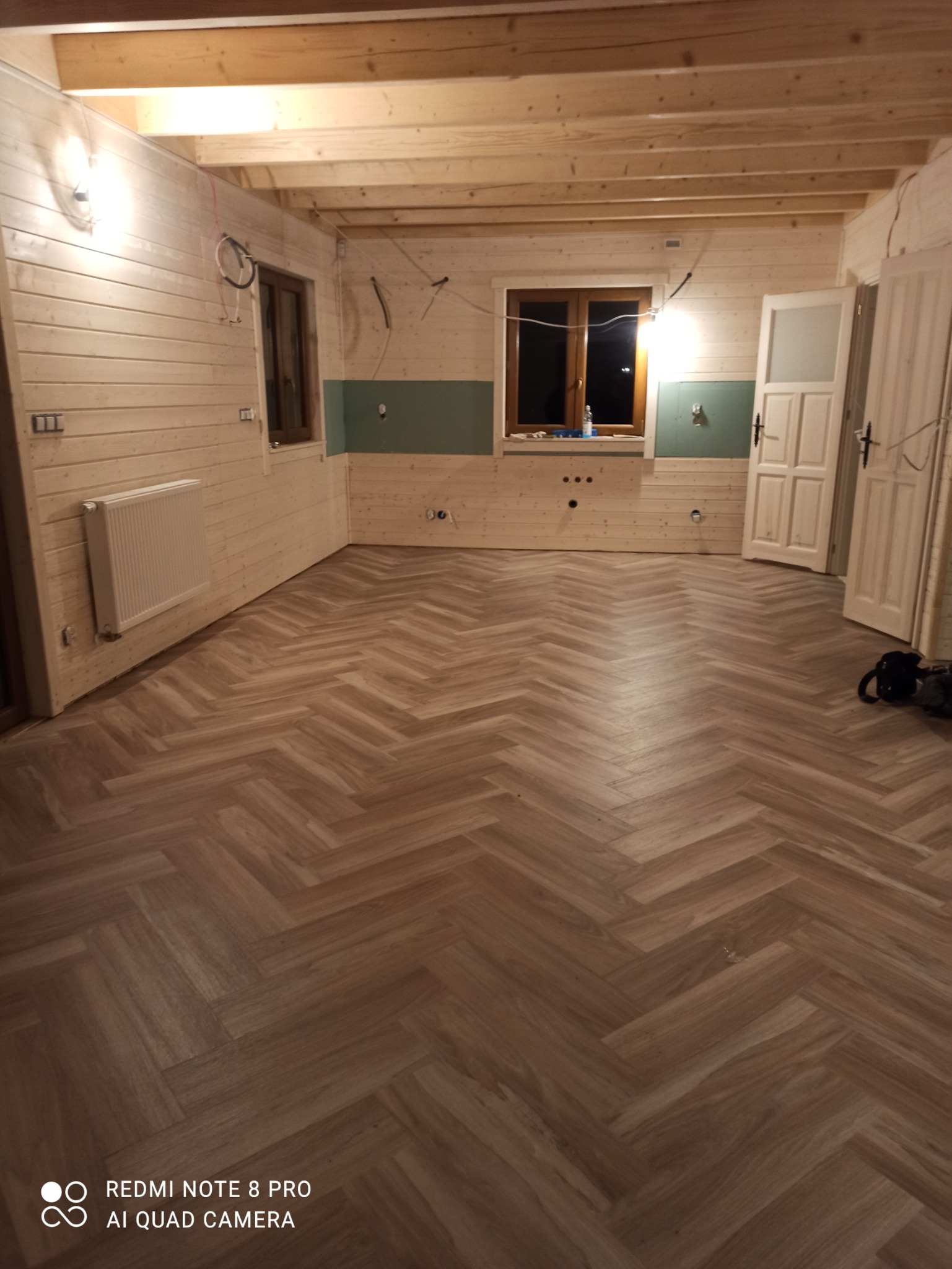 Salon w trakcie wykańczania: drewniane ściany, sufit i podłoga ułożona w jodełkę, widoczne instalacje elektryczne.