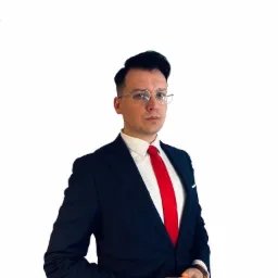 Portret mężczyzny w okularach, granatowym garniturze i czerwonym krawacie, z rękami złożonymi przed sobą, na białym tle.