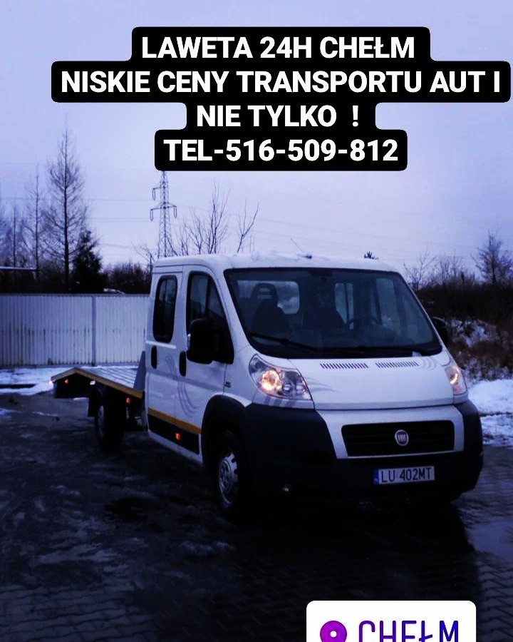 Biała laweta Fiat Ducato z tablicą rejestracyjną LU 402MT, zaparkowana na mokrym, ciemnym asfalcie w pochmurny dzień, z widocznym napisem 'LAWETA 24H Chełm niskie ceny transportu aut i nie tylko!