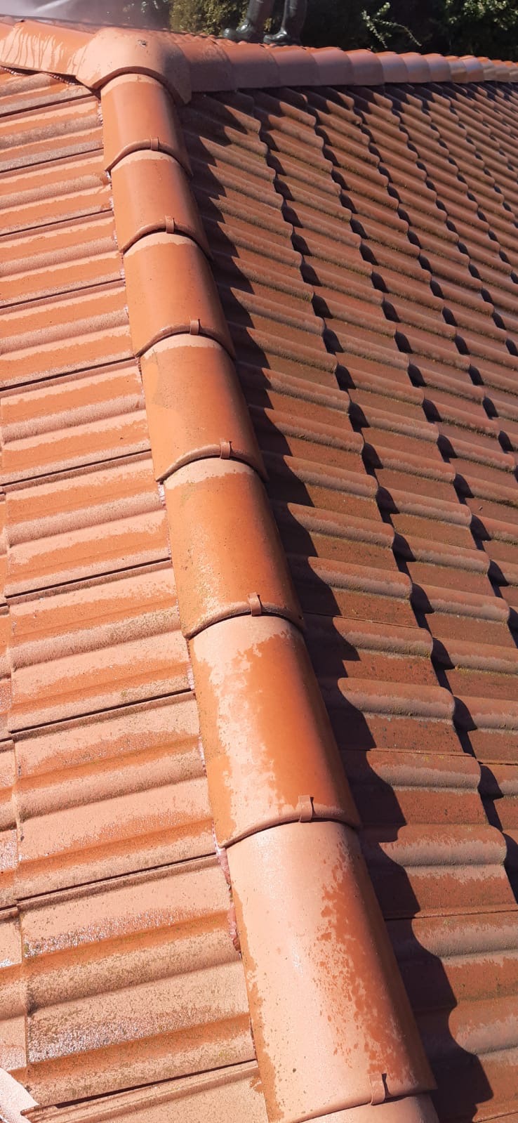 Czerwona dachówka ceramiczna, częściowo umyta, z widocznym brudem i mchem na nieumytych fragmentach, podczas czyszczenia pod ciśnieniem.