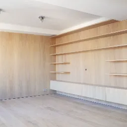 Jasne, drewniane panele ścienne z półkami i szafkami w minimalistycznym stylu, oświetlenie punktowe na suficie.