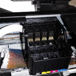 Wnętrze drukarki atramentowej z widocznym wózkiem głowic, elementami elektronicznymi i zaschniętym tuszem na absorberze.