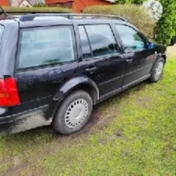 Czarny samochód kombi, prawdopodobnie Volkswagen Golf, zaparkowany na trawie przed domem jednorodzinnym, widok z boku.