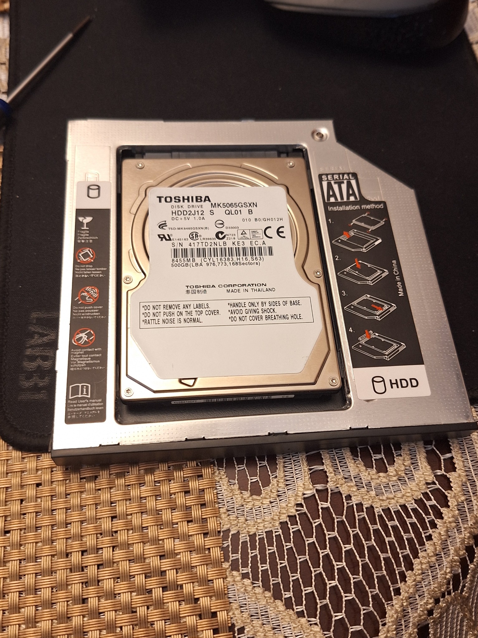Dysk HDD Toshiba 500GB w metalowej ramce montażowej SATA. Widoczne instrukcje instalacji i ostrzeżenia na etykiecie. Drobne elementy i szczegółowe oznaczenia.