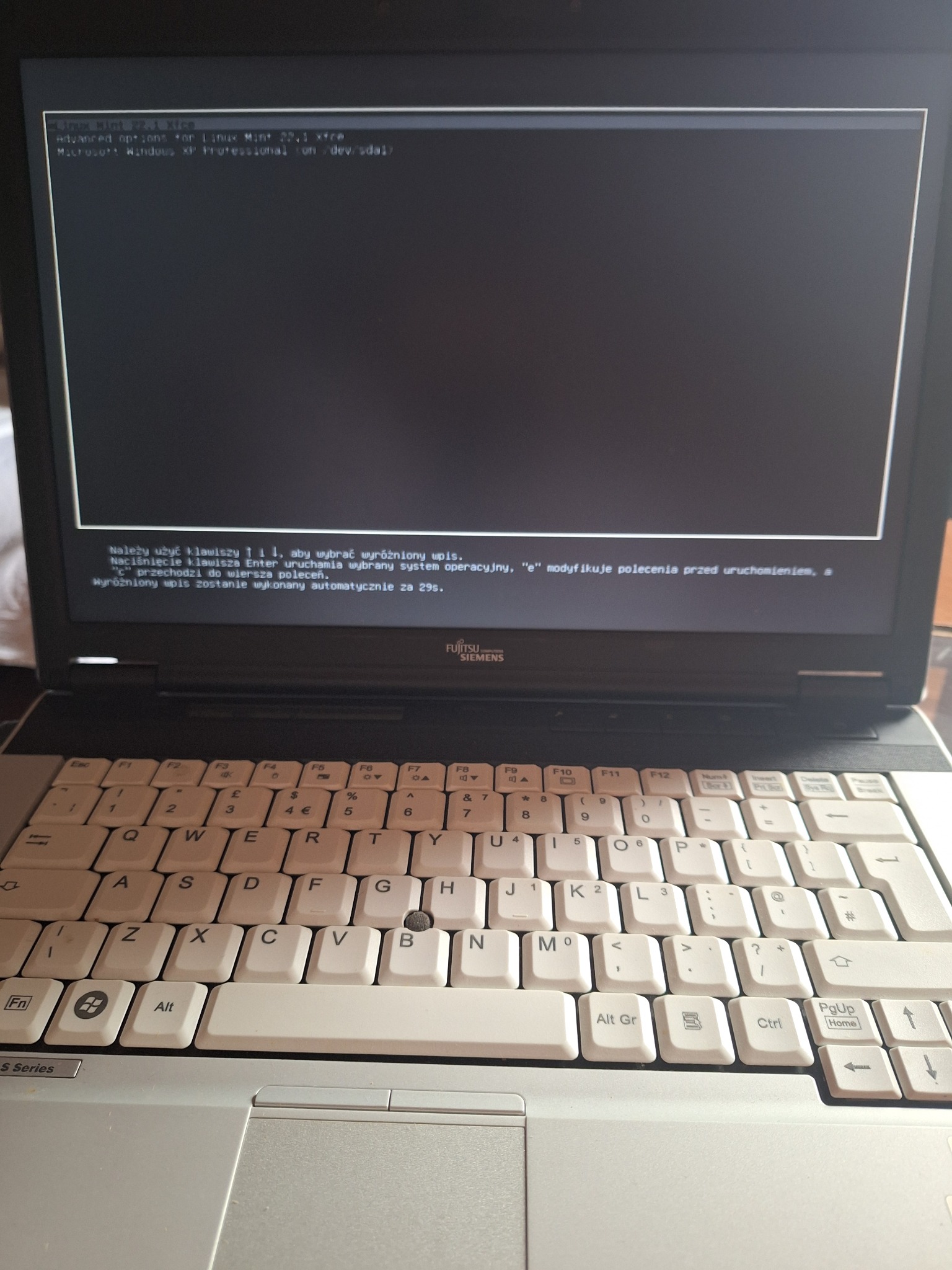 Ekran laptopa Fujitsu Siemens z menu wyboru systemu operacyjnego: Linux Mint 22.1 Xfce i Windows XP. Widoczna klawiatura i touchpad.