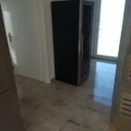 Błyszcząca, beżowo-szara podłoga z kamiennego wzoru po remoncie, widoczne ślady pyłu i niedokładnego sprzątania, w tle czarna szafka na wino i otwarte drzwi balkonowe w jasnym pomieszczeniu.