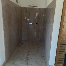 Kabina prysznicowa wyłożona beżowym marmurem z dyszami do hydromasażu, deszczownicą i słuchawką prysznicową, widok z zewnątrz