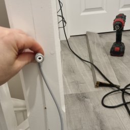 Macrox Ltd - Podłączenie przewodu elektrycznego do ościeżnicy w Rugby podczas remontu, widoczny fragment podłogi z panelami i wiertarka.