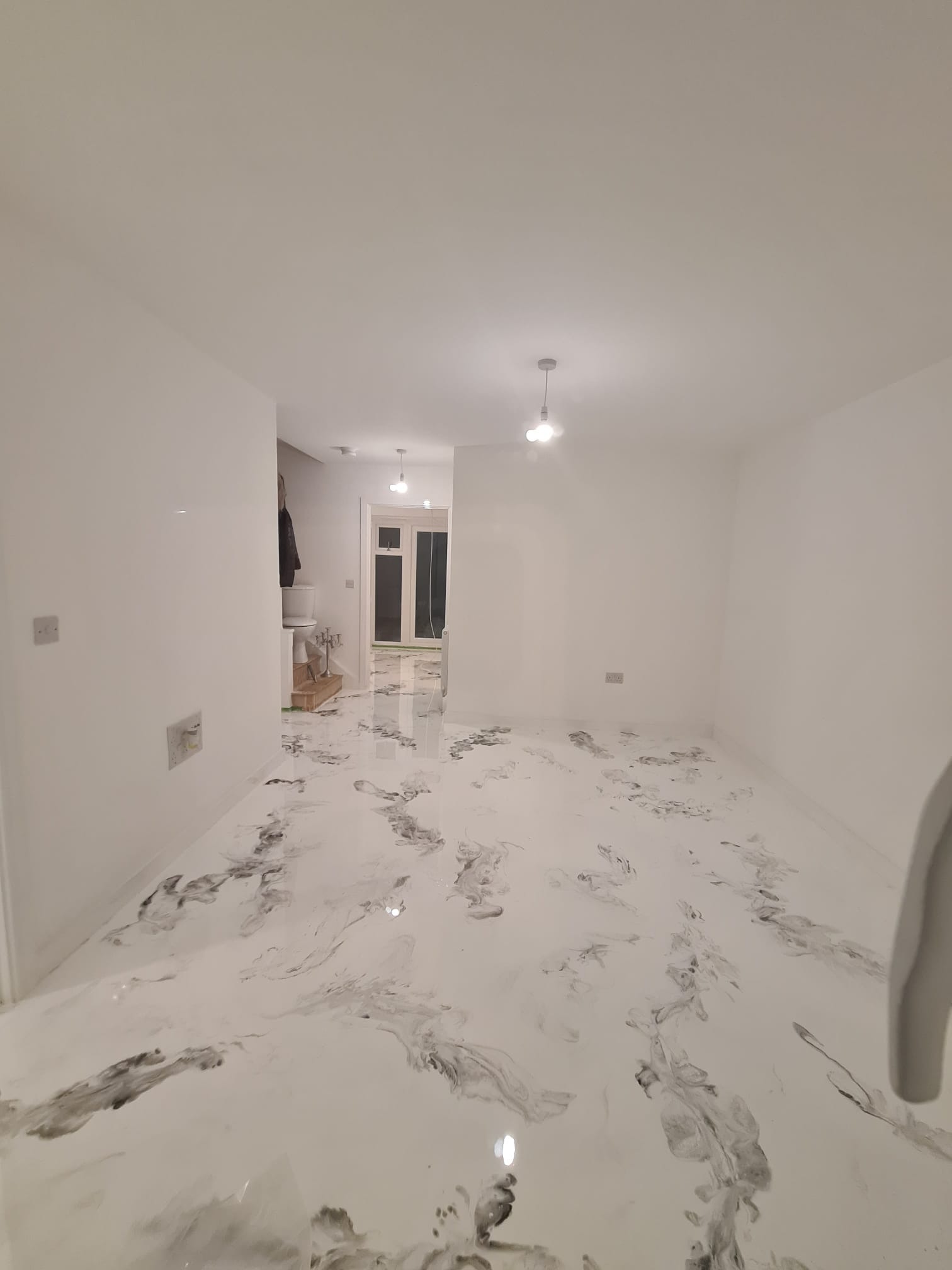 Białe pomieszczenie z podłogą pokrytą żywicą epoksydową z szarymi marmurkowymi wzorami, widok na korytarz z podobnym wykończeniem podłogi.