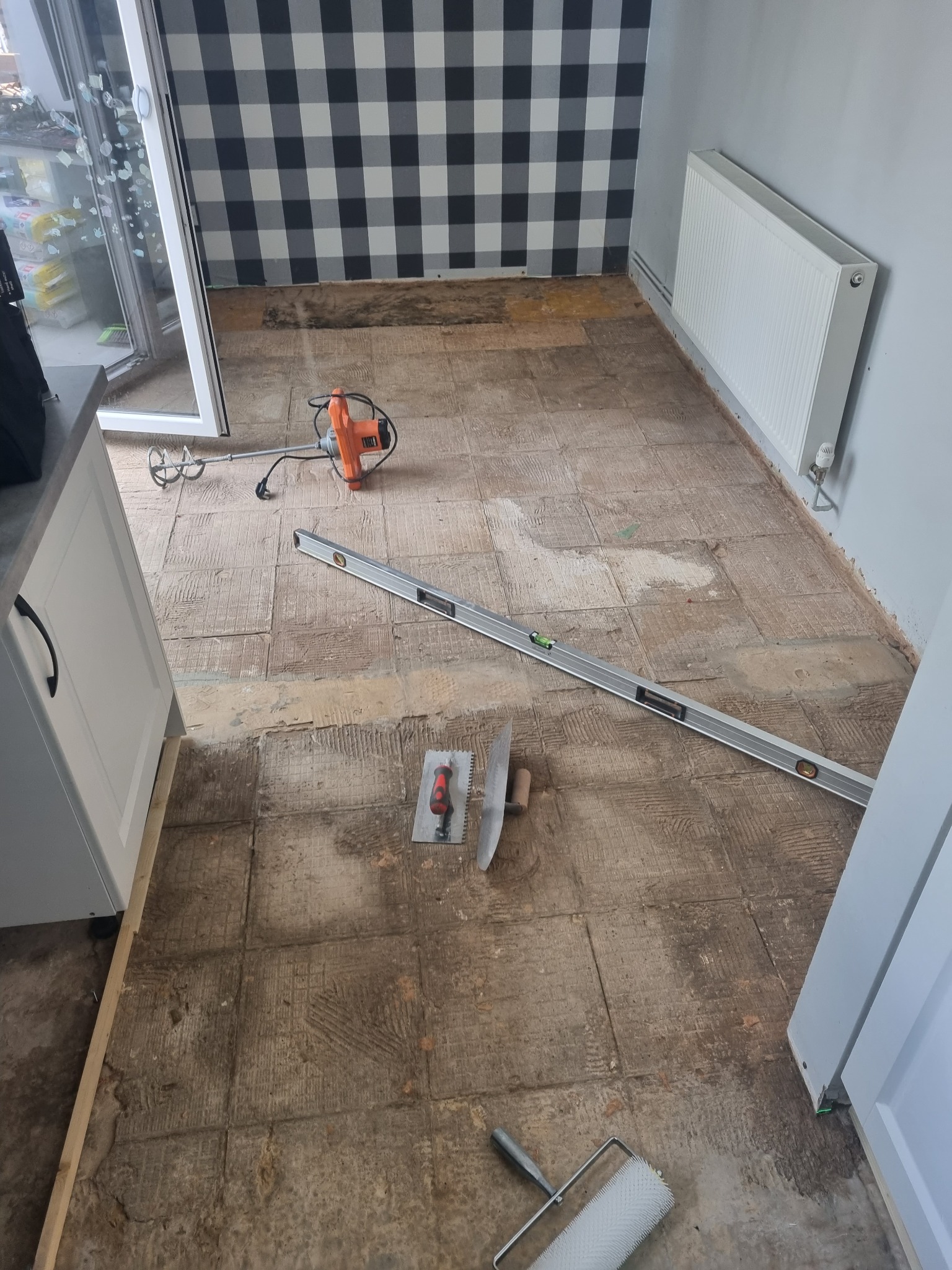 Przygotowanie podłoża pod nową podłogę w kuchni: usunięte stare płytki, widoczny mikser do zaprawy, poziomica, kielnia i wałek kolczasty.