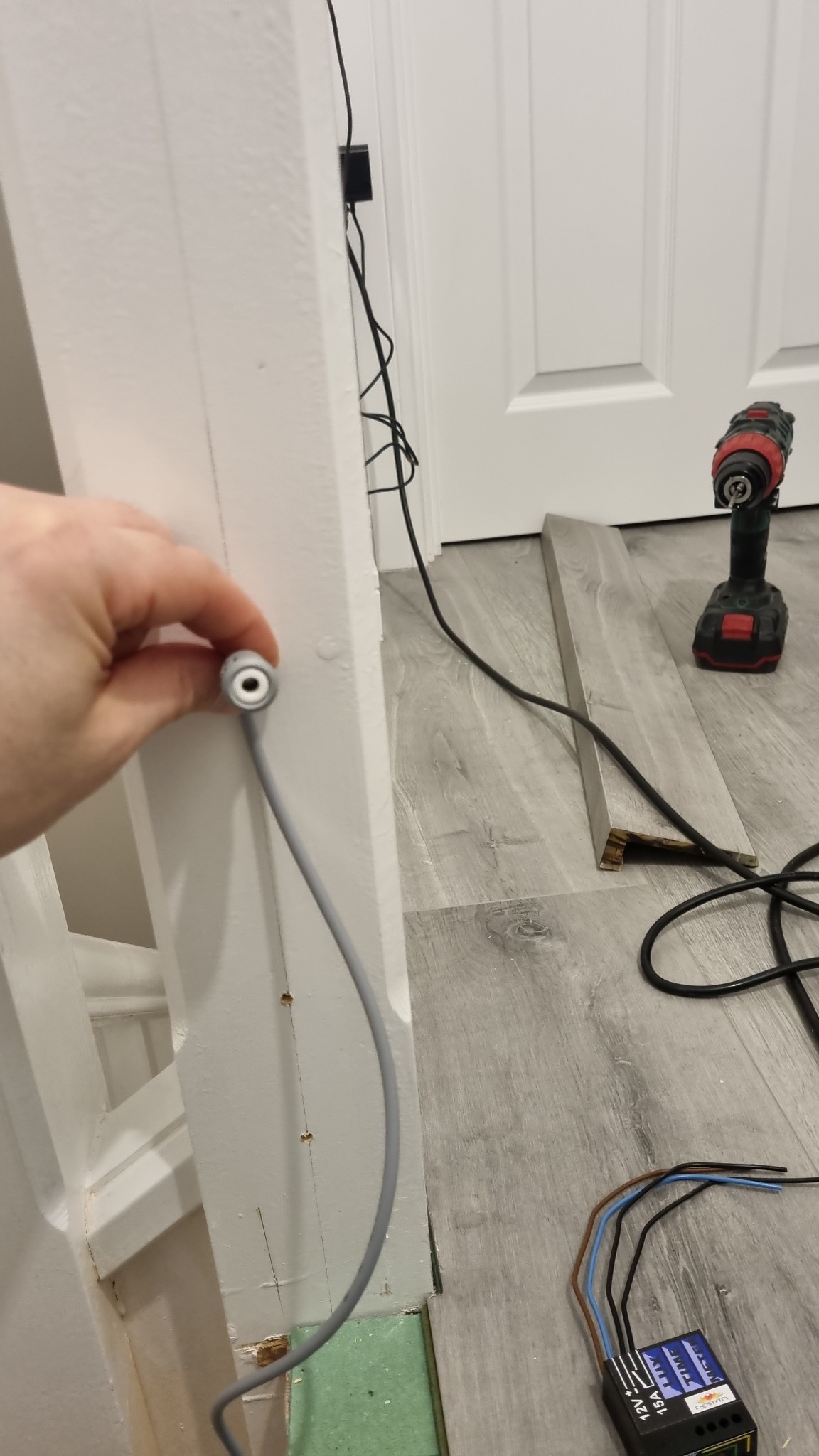 Podłączenie przewodu elektrycznego do ościeżnicy w Rugby podczas remontu, widoczny fragment podłogi z panelami i wiertarka.