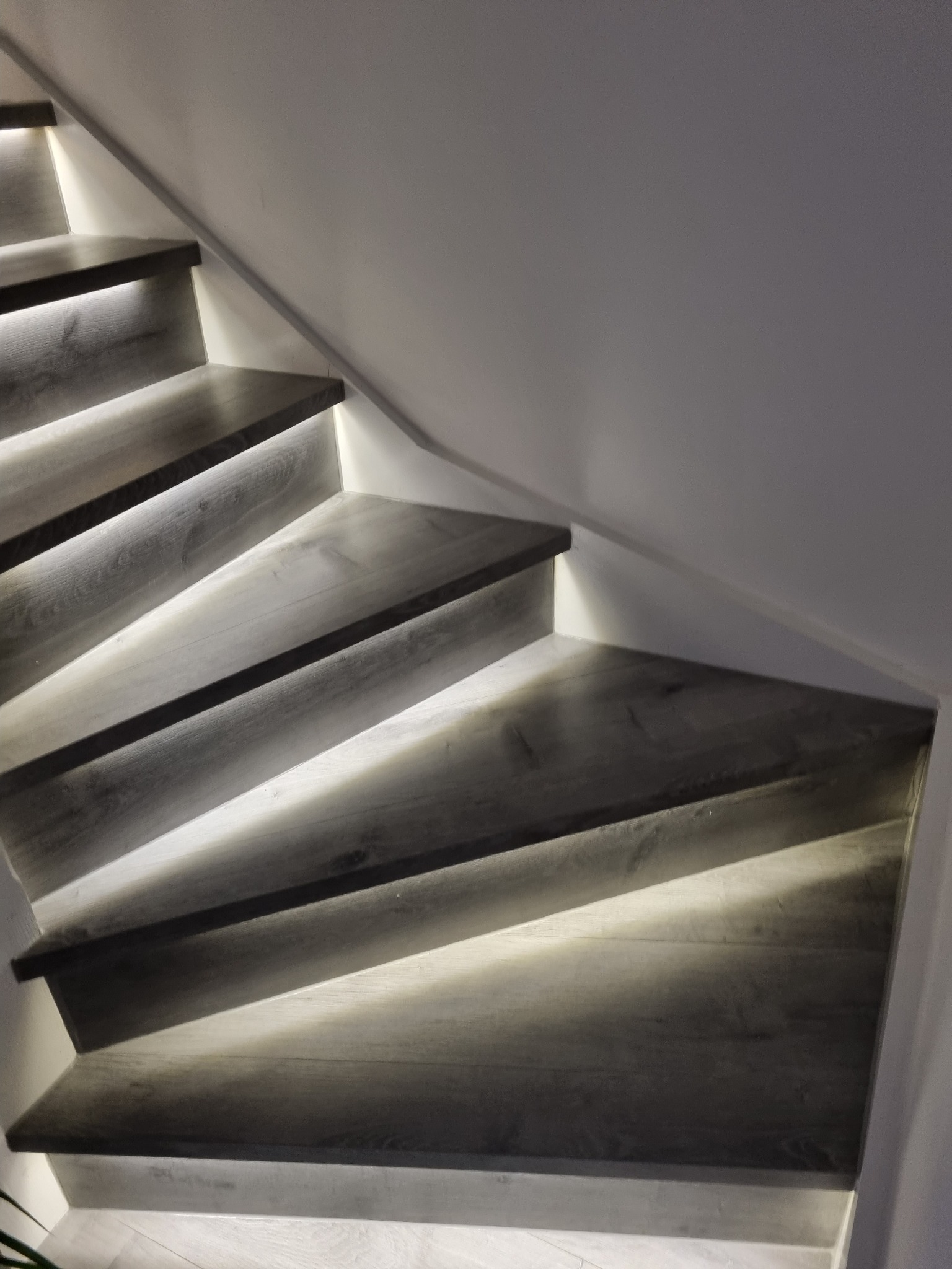 Nowoczesne schody drewniane z podświetleniem LED, widok z dołu, minimalistyczny design.