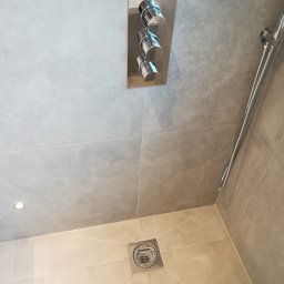 Marcin Rozlepiło - Nowoczesna kabina prysznicowa z szarymi płytkami, chromowaną armaturą i odpływem liniowym w rogu.