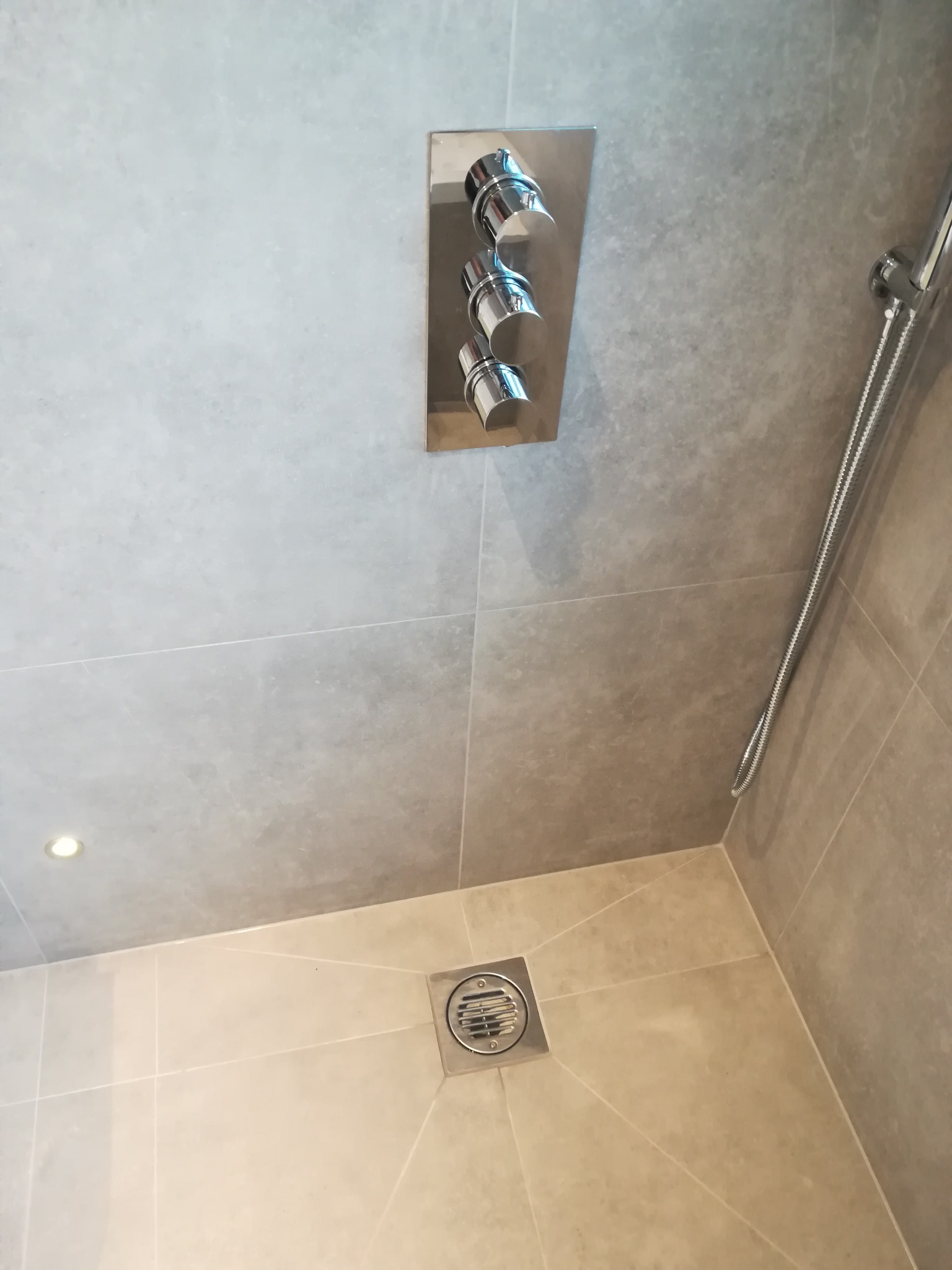 Nowoczesna kabina prysznicowa z szarymi płytkami, chromowaną armaturą i odpływem liniowym w rogu.