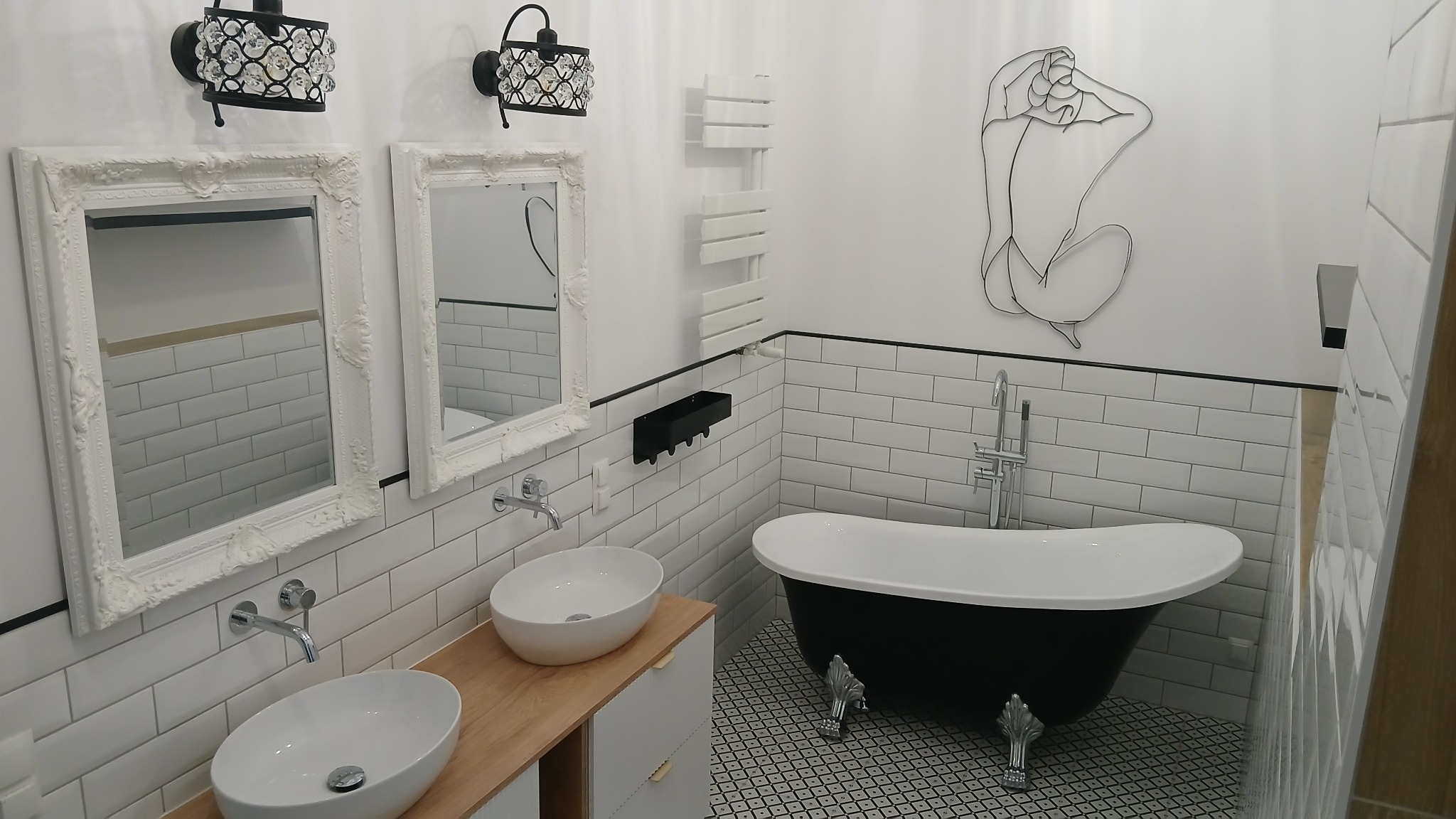 Nowoczesna łazienka w stylu retro z czarno-białą wolnostojącą wanną na ozdobnych nóżkach, dwoma umywalkami nablatowymi na drewnianym blacie, białymi lustrami w ozdobnych ramach i dekoracją ścienną...