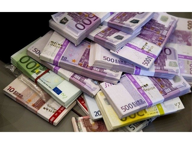 Stosy banknotów Euro o różnych nominałach (10, 20, 100, 500) przewiązane banderolami, ułożone chaotycznie na ciemnym tle.