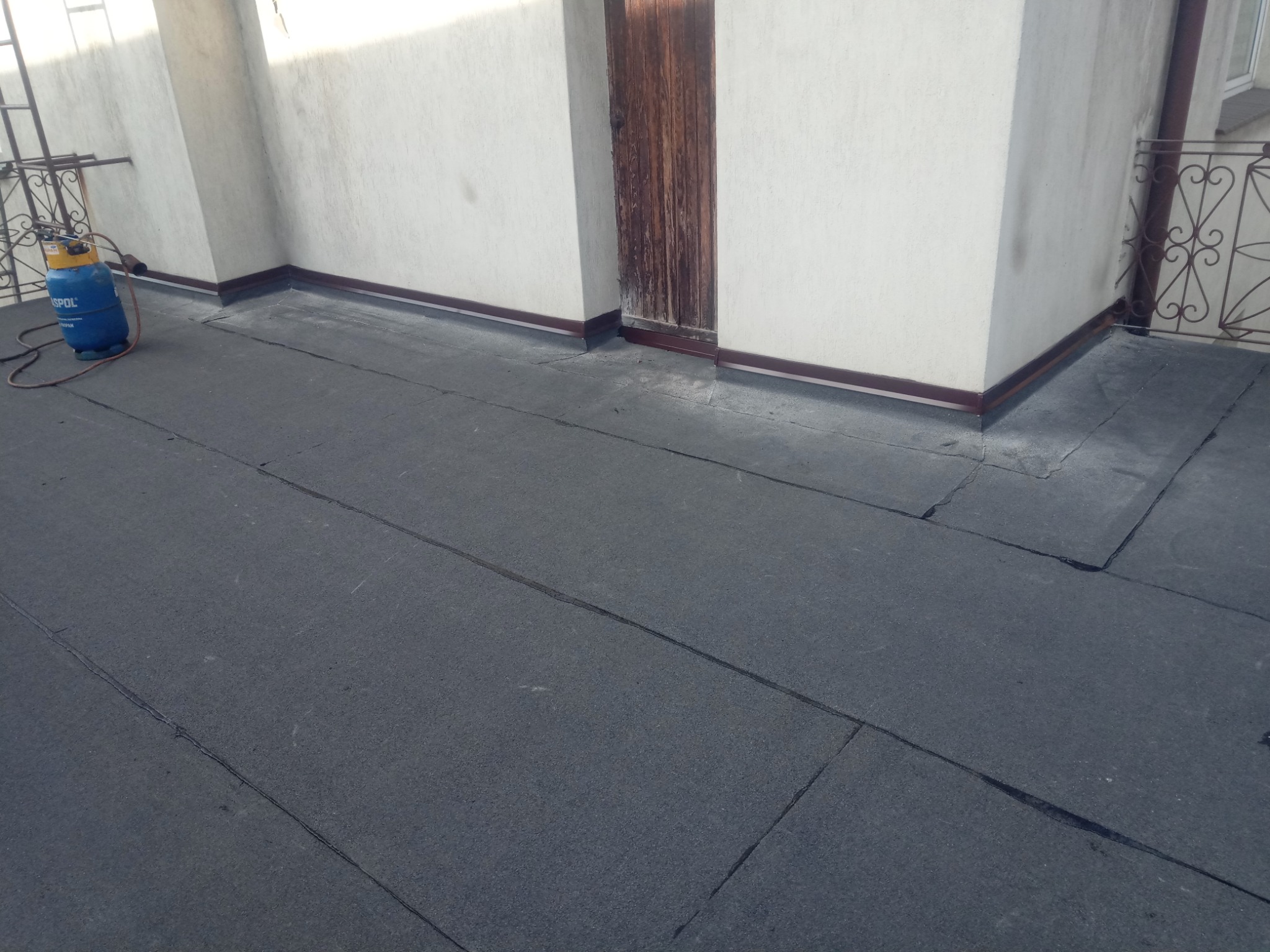 Wykończony płaski dach pokryty papą termozgrzewalną, widoczny butla gazowa i drabina przy ścianie budynku.