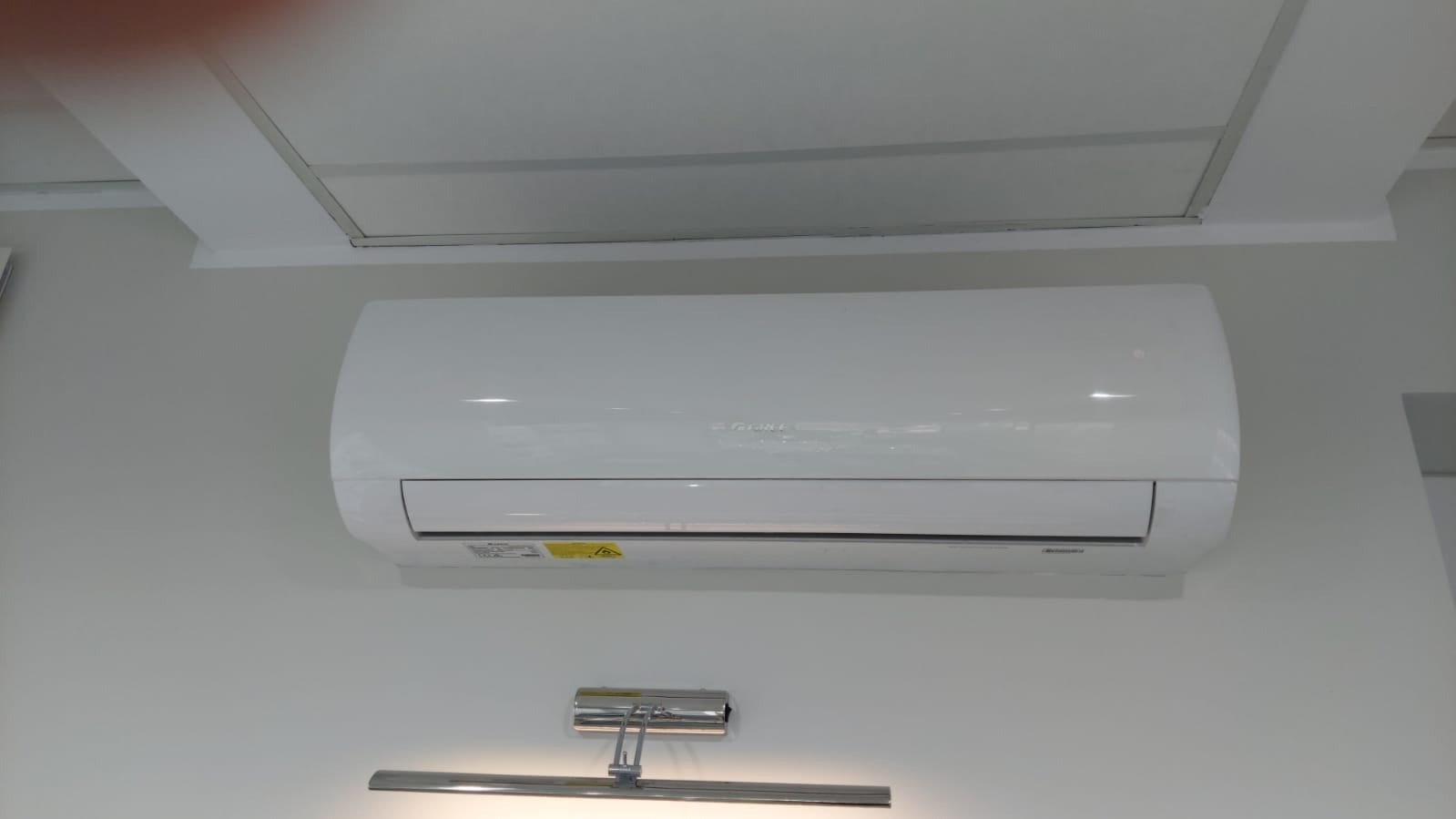 Biała klimatyzacja Gree MUSE zamontowana na ścianie w pomieszczeniu z oświetleniem punktowym.