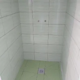 Wykończony prysznic z zielonymi płytkami ceramicznymi na ścianach i podłodze, widoczny odpływ liniowy oraz dwa punkty podłączenia baterii.