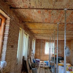 WJ Waszka - Surowe ceglane ściany i sklepiony sufit z widocznymi pęknięciami, podparty rzędem metalowych stempli w remontowanym wnętrzu. Na podłodze materiały budowlane.