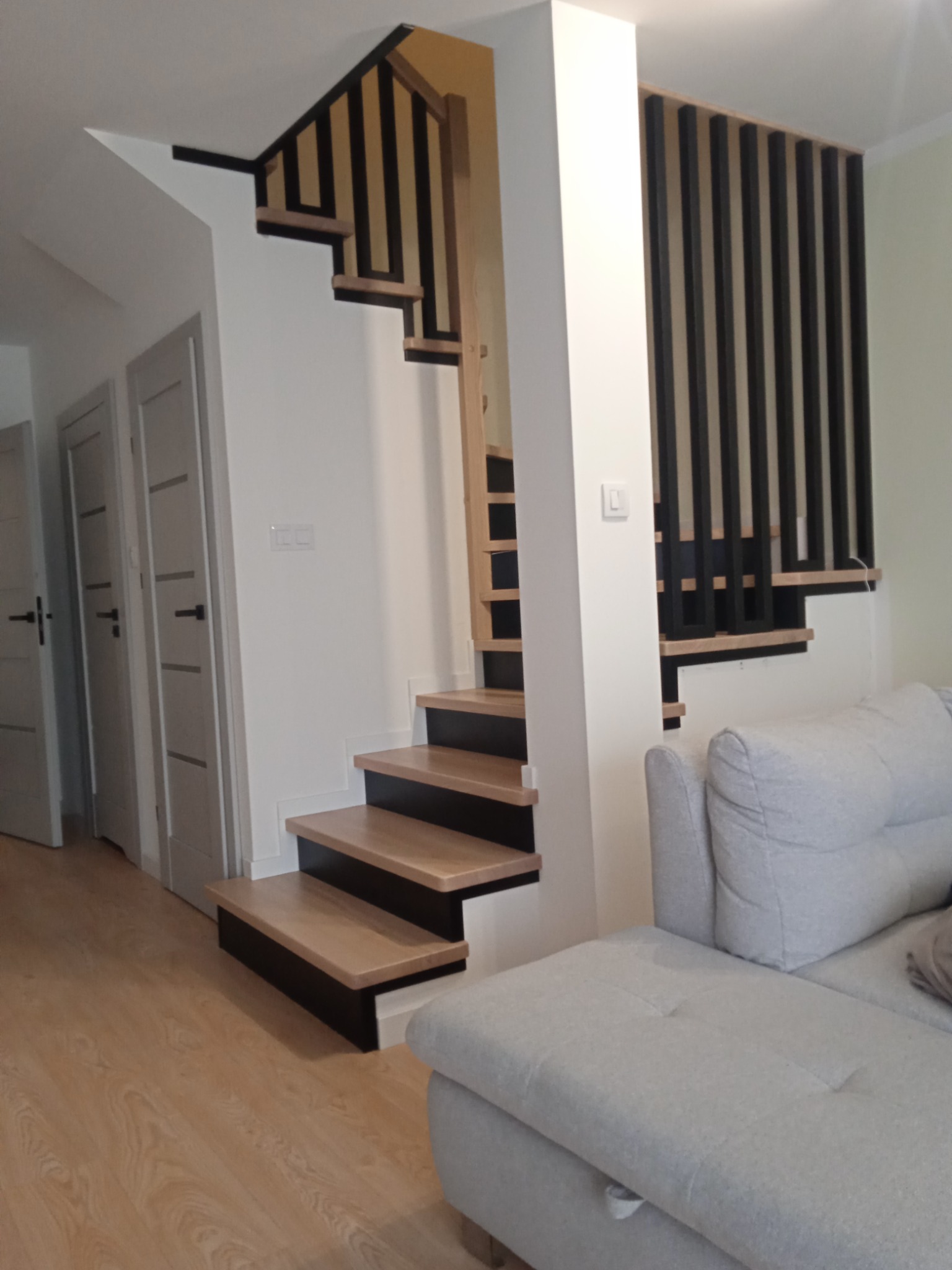 Nowoczesne schody z drewnianymi stopniami i czarną balustradą w jasnym wnętrzu, widok z dołu.