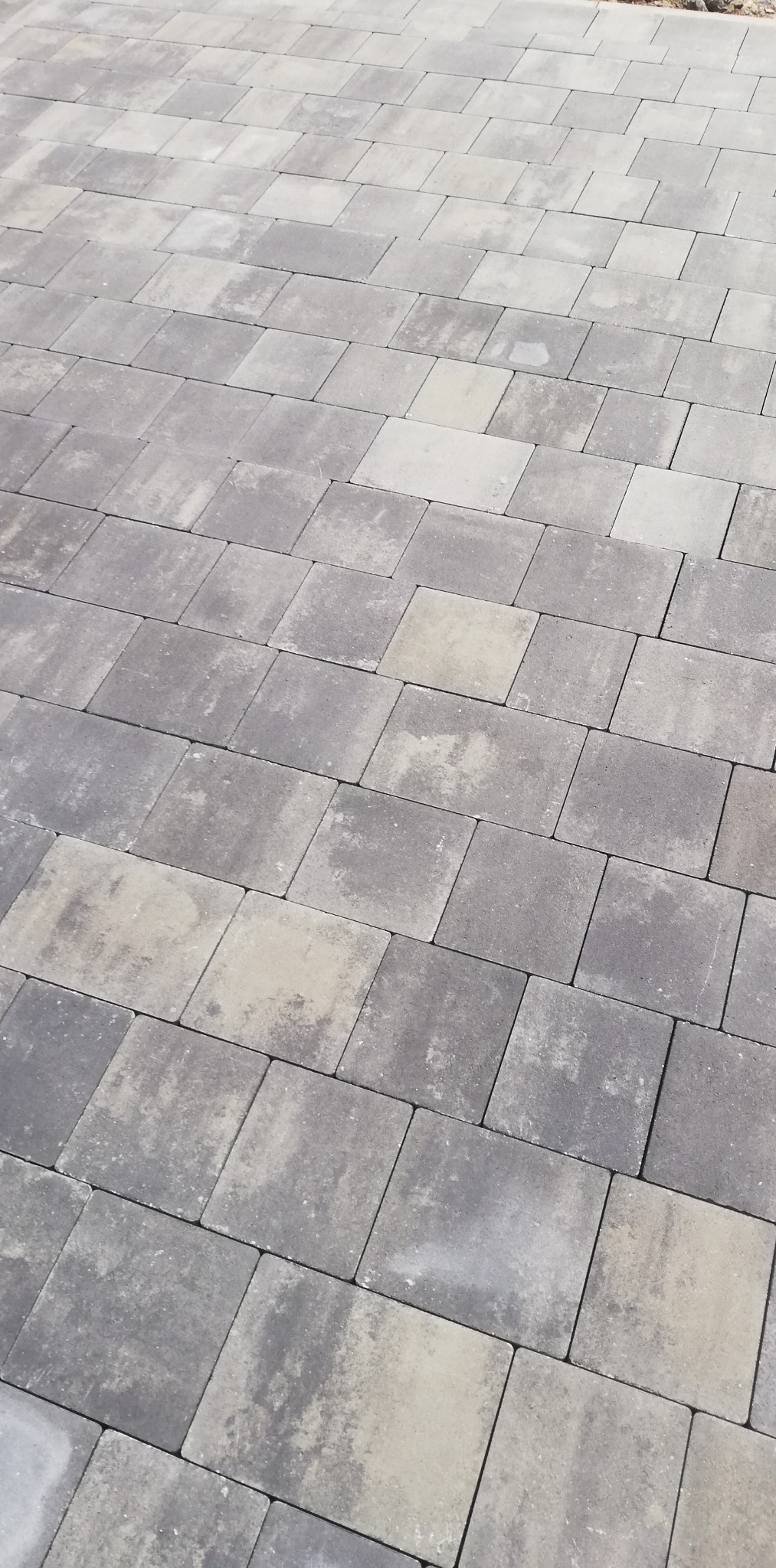 Ułożona szara kostka brukowa o nieregularnym wzorze, widoczna z perspektywy ukośnej, z lekkim przebarwieniem na niektórych elementach.
