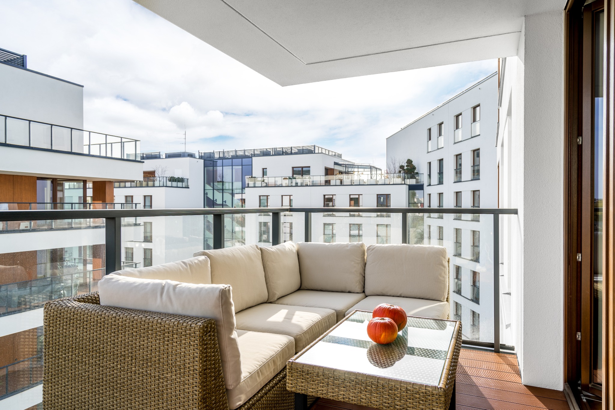 Nowoczesny balkon z rattanowym narożnikiem, szklanym stolikiem i dwoma dyniami na tle zabudowy miejskiej.