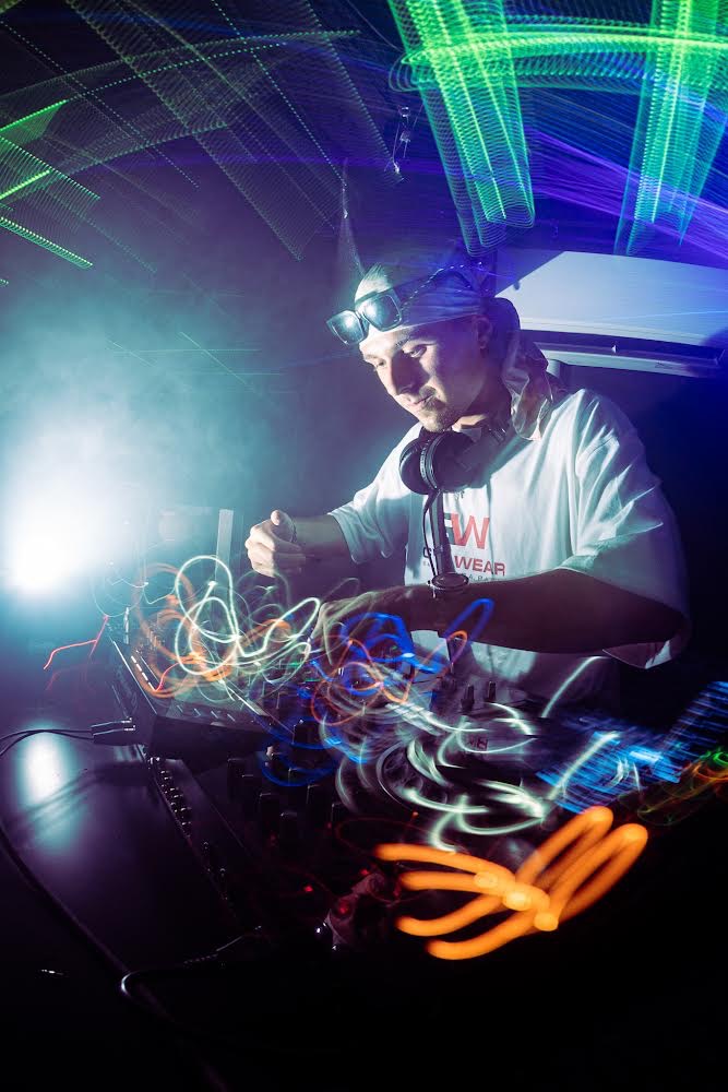 DJ z Wrocławia w trakcie występu, oświetlenie sceniczne tworzy abstrakcyjne wzory, widoczny mikser i słuchawki.