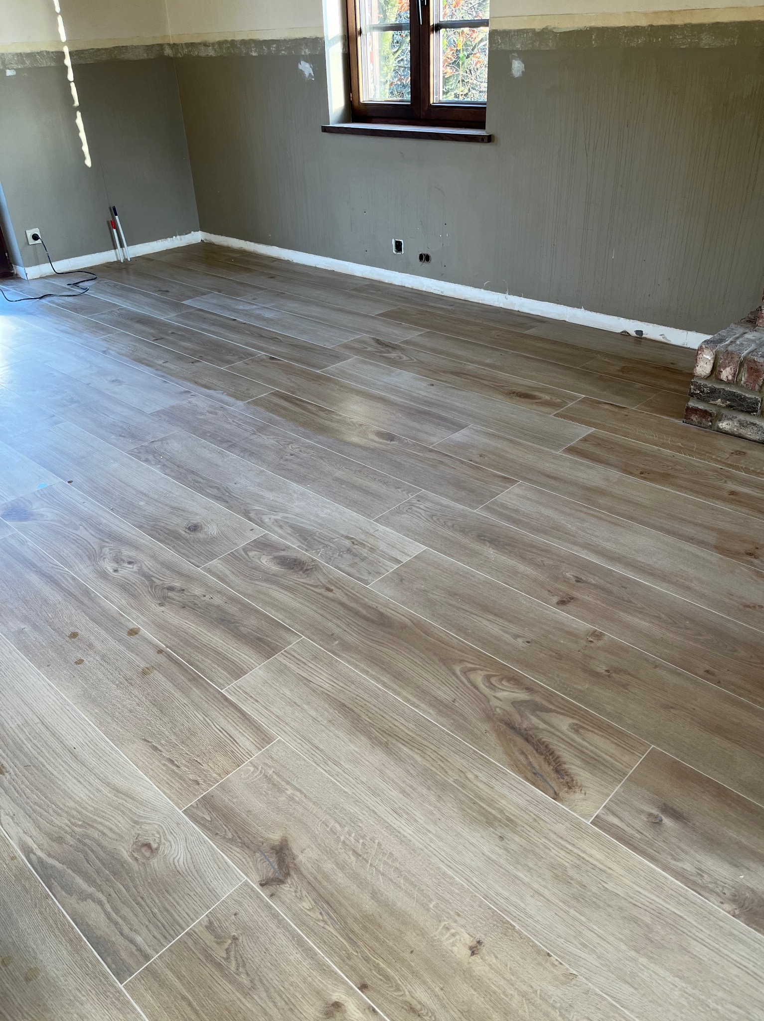 Ułożona podłoga z płytek imitujących drewno w pokoju przed wykończeniem ścian, widoczne ślady po pracach remontowych.
