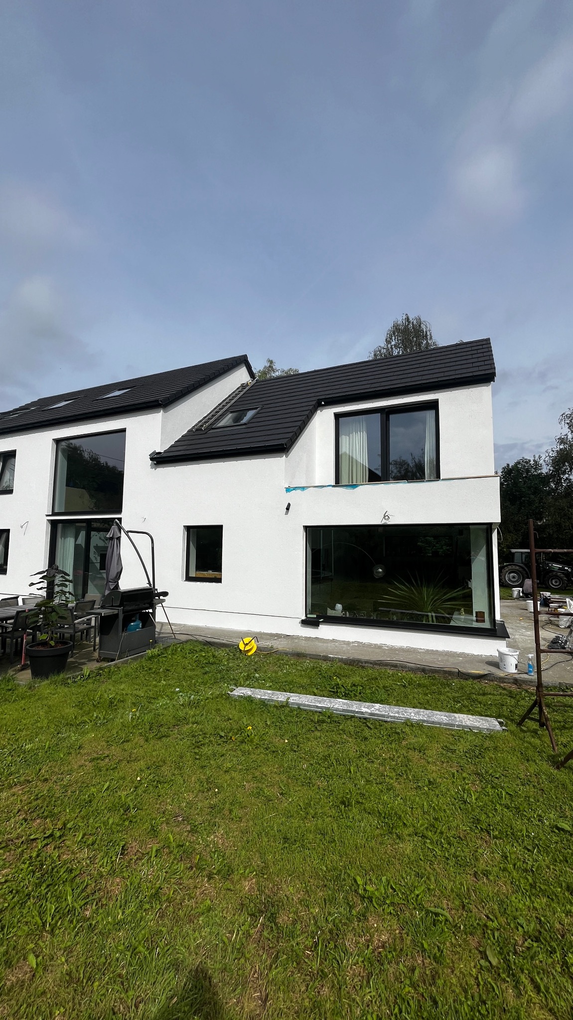 Nowoczesny dom z białymi ścianami i czarnymi ramami okiennymi w Białymstoku, widok z ogrodu, widoczne ślady po pracach wykończeniowych elewacji oraz narzędzia.