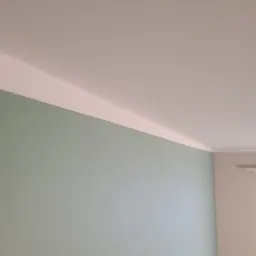 Świeżo pomalowana ściana w odcieniu pastelowej zieleni, z widoczną linią łączenia z białym sufitem, ukazująca gładkie wykończenie powierzchni.