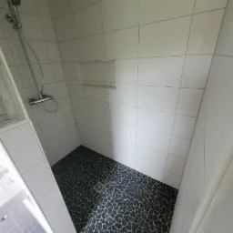 Wykończona kabina prysznicowa w Wołowie z czarną mozaiką na podłodze i białymi płytkami na ścianach, widoczny odpływ liniowy i bateria prysznicowa.